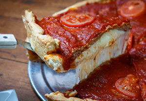 A slice of Sonny’s Italian Kitchen & Pizzeria deep-dish pizza being lifted, cheese stretching.