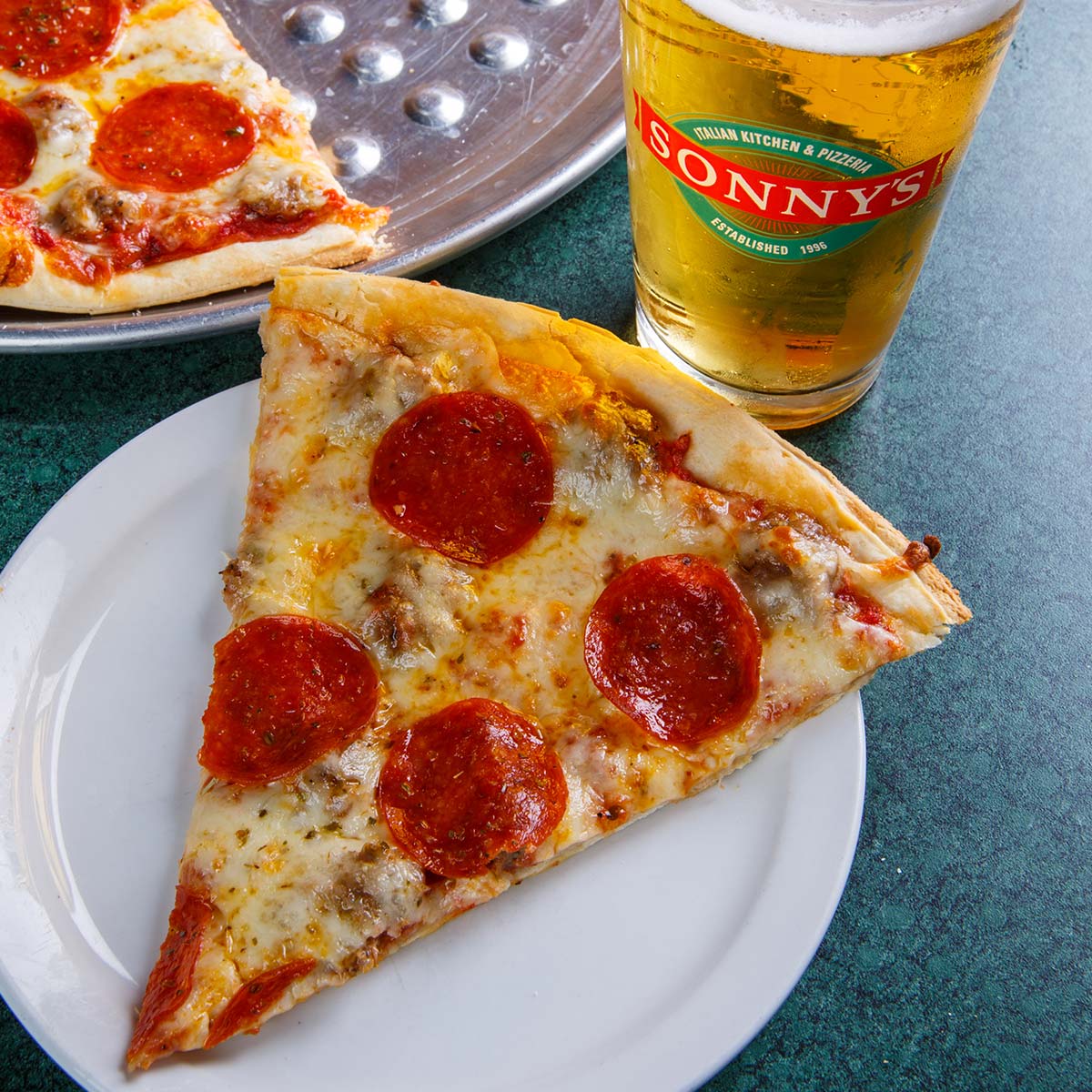 A slice of pizza from Sonny’s Italian Kitchen & Pizzeria with beer, perfect waterfront dining.