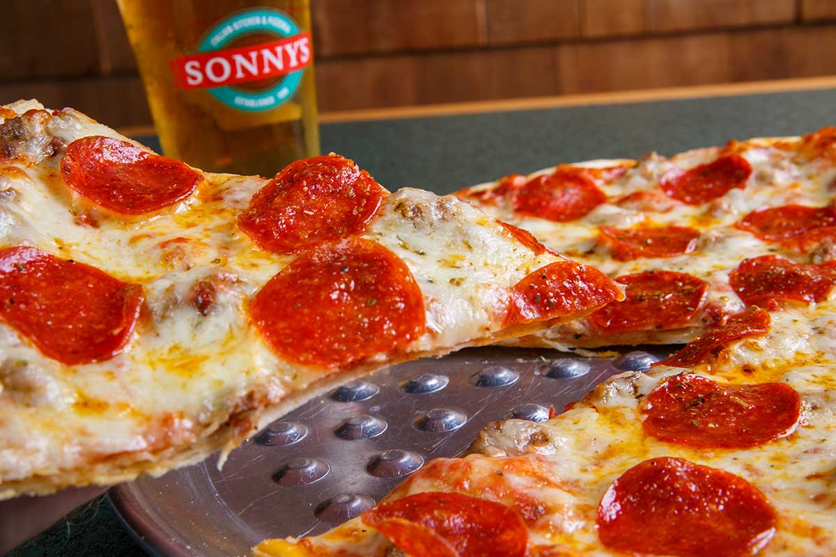 A slice of pepperoni pizza at Sonny’s Italian Kitchen & Pizzeria, drink glass in background.