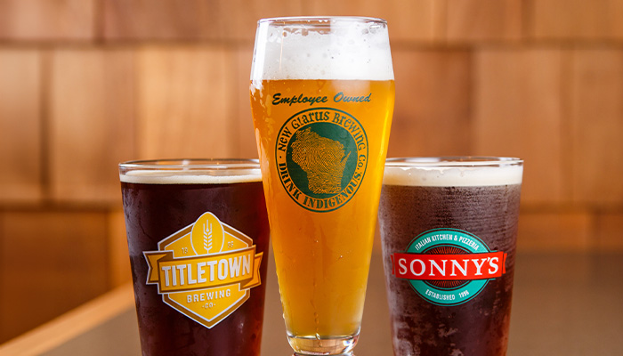 Three beers with brewery logos sit on a wooden table at Sonny’s Italian Kitchen & Pizzeria.