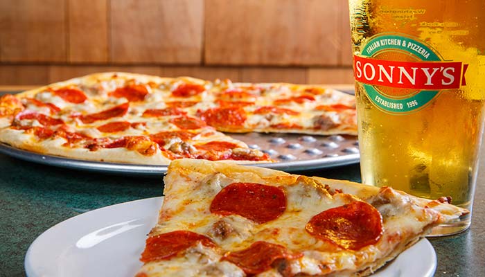 Pepperoni pizza slice on a plate, Sturgeon Bay beer, and a pizza in Door County in the background.